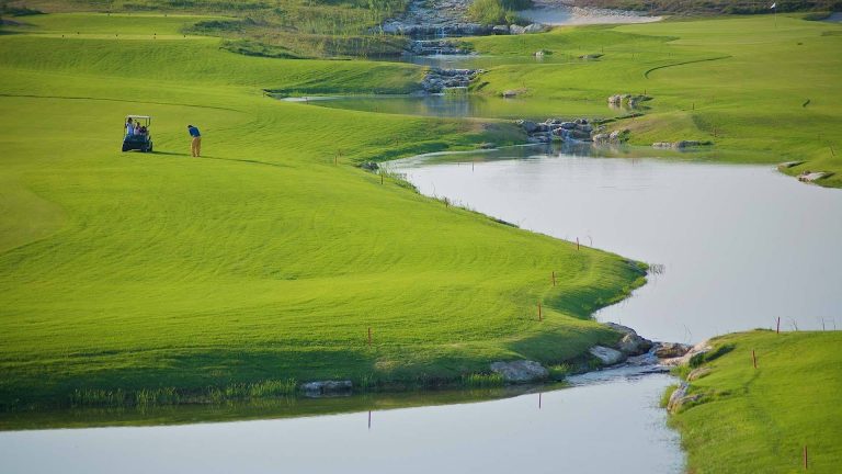 A fairway curving around water on the course at Acaya Golf Club, Salento