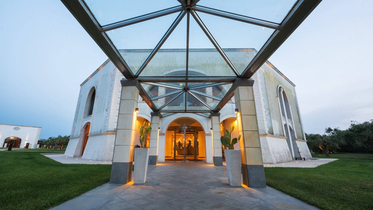The illuminated glass-canopy entrance to Acaya Golf Resort at dusk