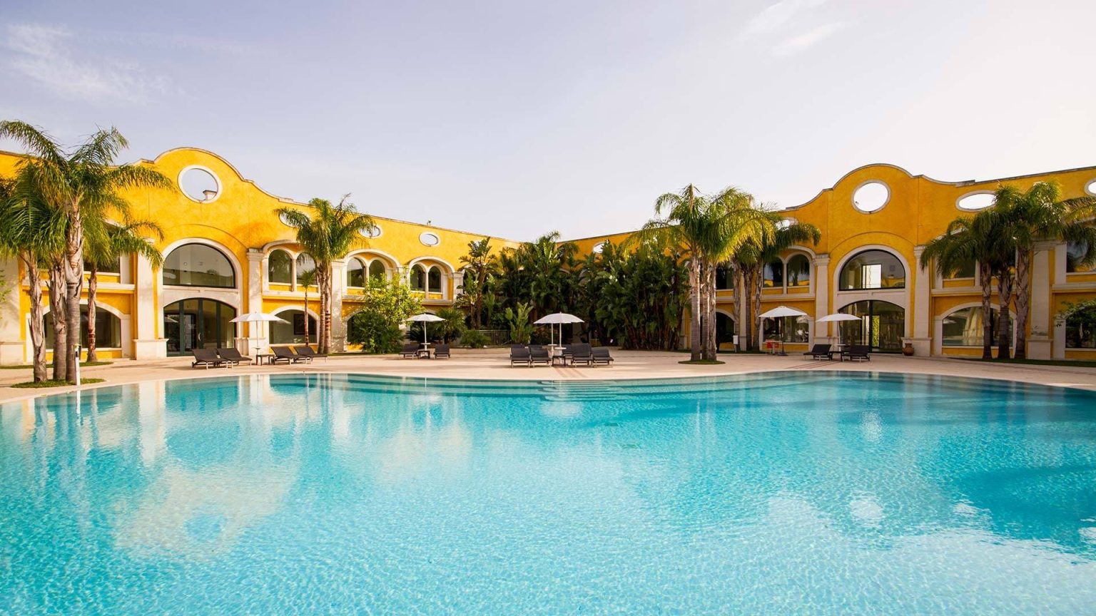 The ochre-yellow facade and main outdoor pool at Acaya Golf Resort, Salento