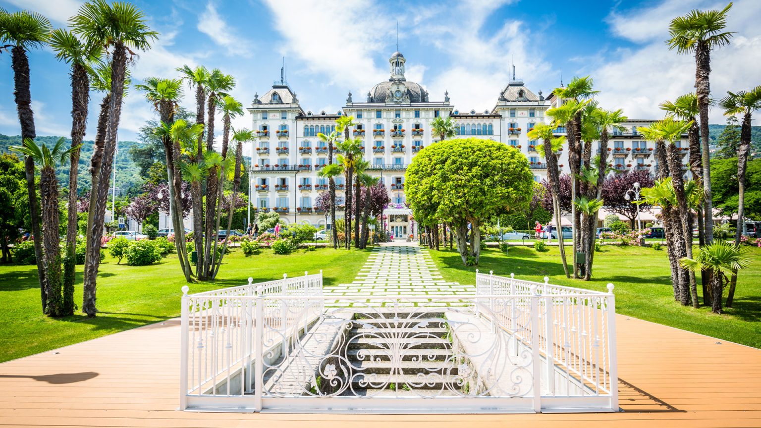 The hotel facade seen from the front garden, framed by palms and a white balustrade