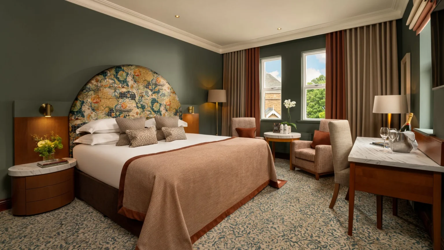 A green-walled bedroom at Culloden Estate and Spa with a tapestry headboard and garden view