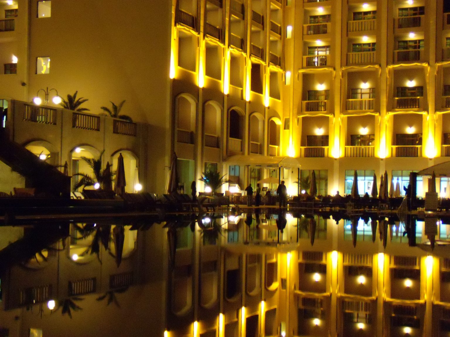 The gold-lit facade of Melia Grand Hermitage reflected in the pool at night